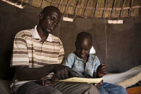 Thesame and his father John inside their tuku at a refugee settlement in Adjumani. Photo: Hugh Rutherford /Finn Church Aid.