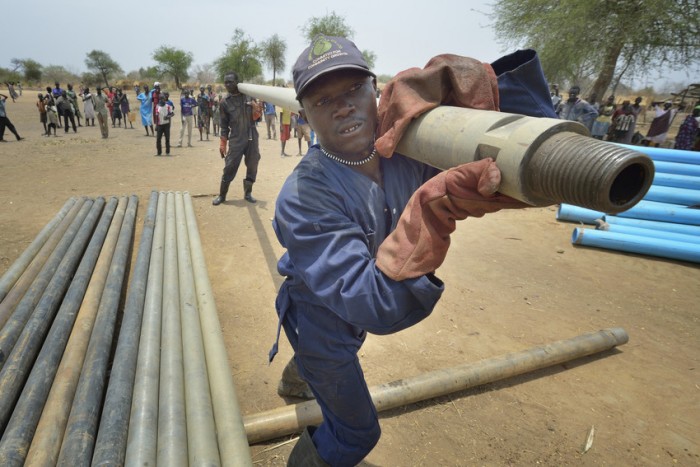 Workers carry pipe as they drill a well on April 7, 2017, in Rumading, a village in South Sudan's Lol State where more than 5,000 people, displaced by drought and conflict, remain in limbo. In early 2017, they set out walking for Sudan, seeking better conditions, but were stopped from crossing the border. They remain camped out under the trees at Rumading, eating wild leaves as the rainy season approaches. In early April, Norwegian Church Aid, a member of the ACT Alliance, began drilling the well in the informal settlement and distributed sorghum, beans and cooking oil to the most vulnerable families. The ACT Alliance is carrying out the emergency assistance in coordination with government officials and the local Catholic parish. South Sudan. Photo: Paul Jeffrey/ACT