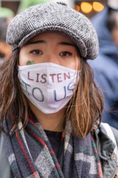 Photo of a woman in a mask reading "Listen to us"